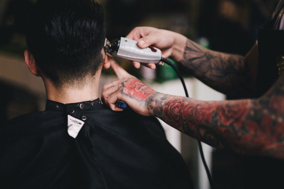 Tattooed barber uses clippers on customers hair